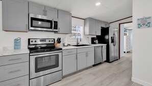 A modern kitchen with stainless steel appliances, grey cabinetry, and a white countertop. - Easy living lodge, large yard and parking area-heart of Murrells Inlet (Murrells Inlet)