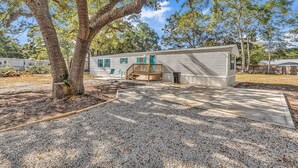 A single-story house with a covered porch, a small deck, and a gravel driveway. - Easy living lodge, large yard and parking area-heart of Murrells Inlet (Murrells Inlet)