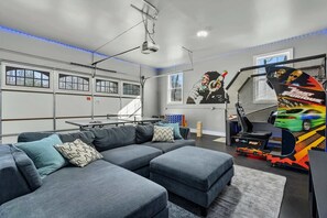 Uma sala de estar moderna com um sofá seccional, um projetor e uma área de jogos com fliperama de tema automotivo.