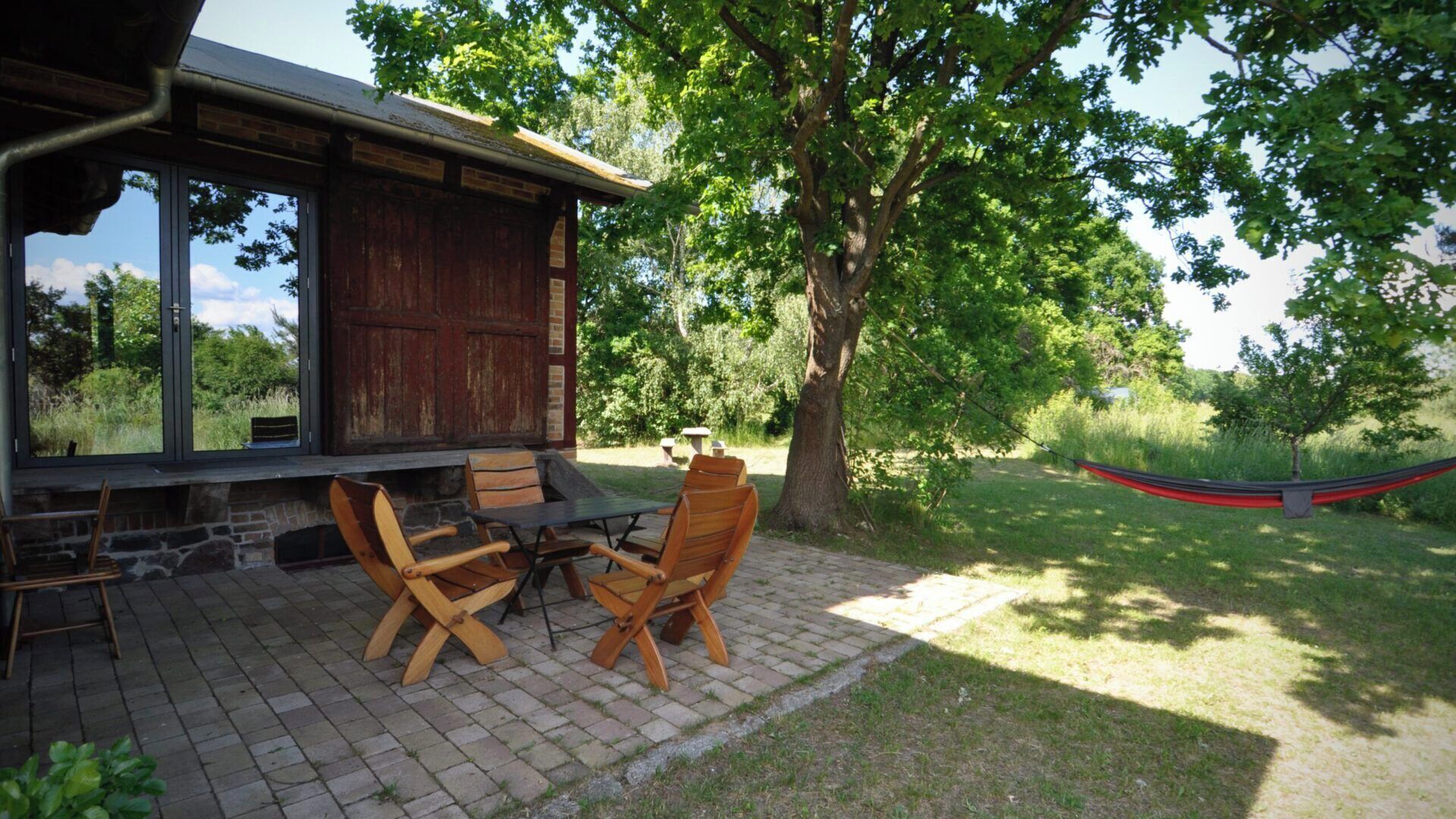 A rustic outdoor seating area with wooden chairs and a table, a hammock, and a view of a lush green landscape.
