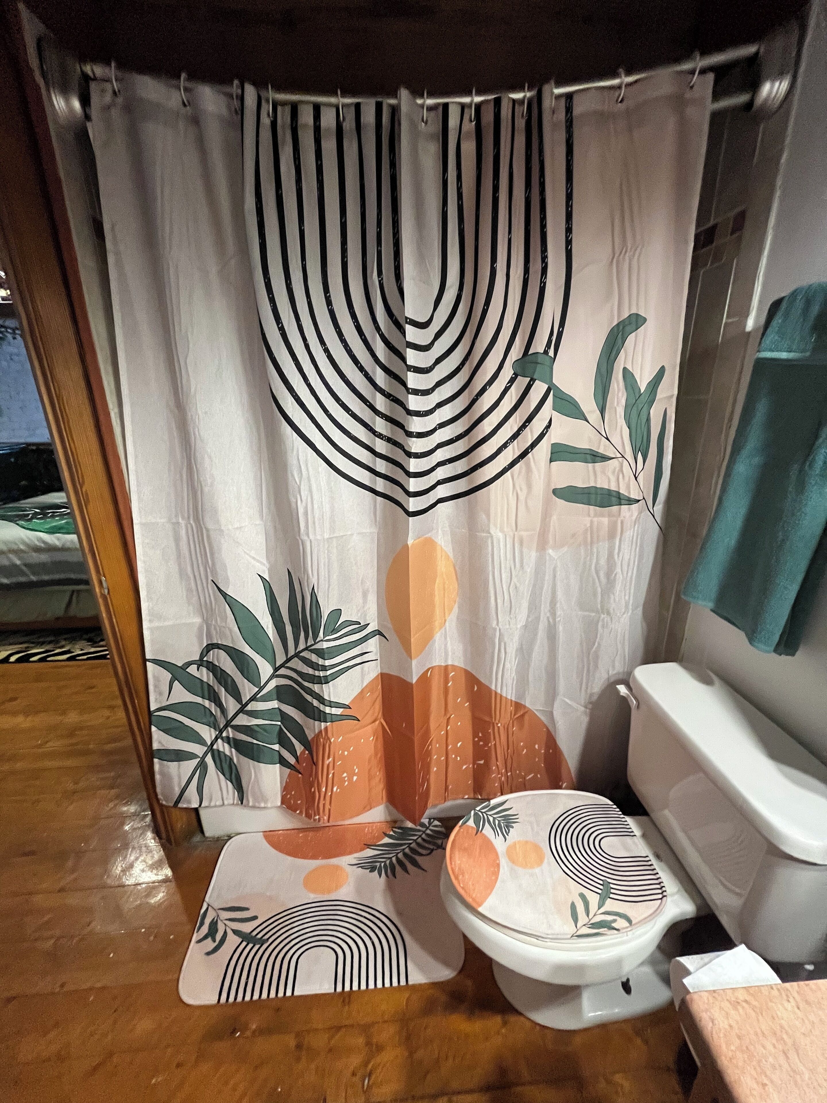 Une salle de bain avec des toilettes, un rideau de douche orné de motifs de feuilles et un plancher en bois.