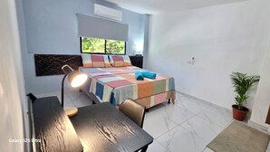 A small, modern room with a bed, a desk, and a potted plant.