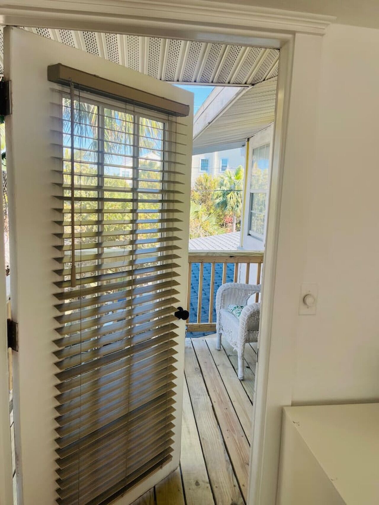 Una puerta con persianas horizontales, una terraza de madera y una silla blanca en un balcón.