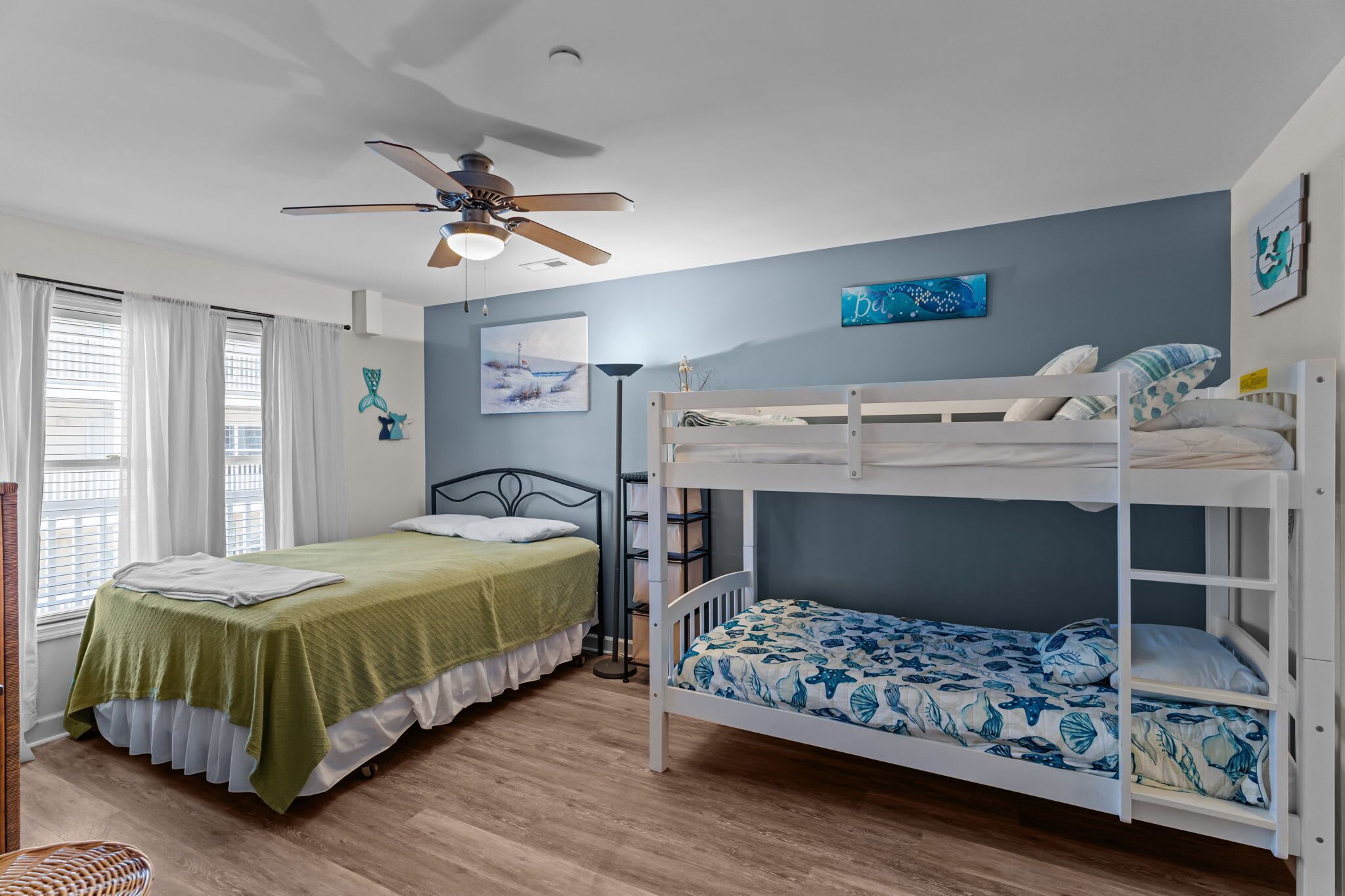 Una camera da letto con un letto a castello, un letto singolo, una ventola a soffitto e vista sul mare dalla finestra.