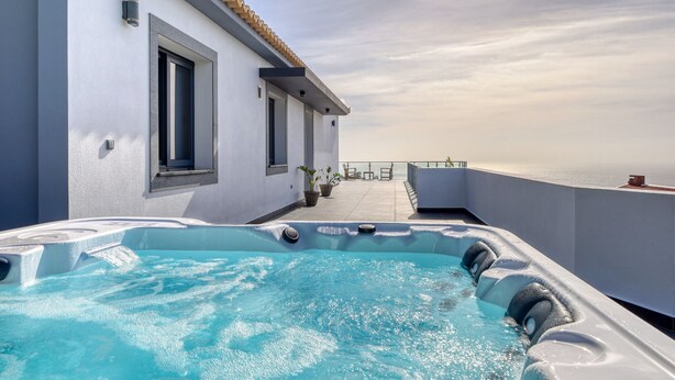 Un área de piscina en la azotea con un jacuzzi, una terraza con vistas al mar y un edificio con tejado de baldosas.