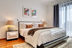 A modern bedroom with a large bed, two bedside tables, a nightstand, a window with sheer curtains, and two framed floral artworks on the wall. - Oasis do Sol, a Home in Madeira (Ponta do Sol)