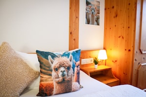 Una cama con un almohadón de alpaca, una lámpara de noche y una pared de madera.