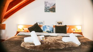 Een slaapkamer met een houten plafond, een bed met een vachtdeken, twee kussens, en een schilderij van een berglandschap aan de muur.
