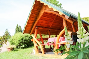 Eine Holzhütte mit einem geneigten Dach, einer Bank und einem Tisch mit karierter Tischdecke.
