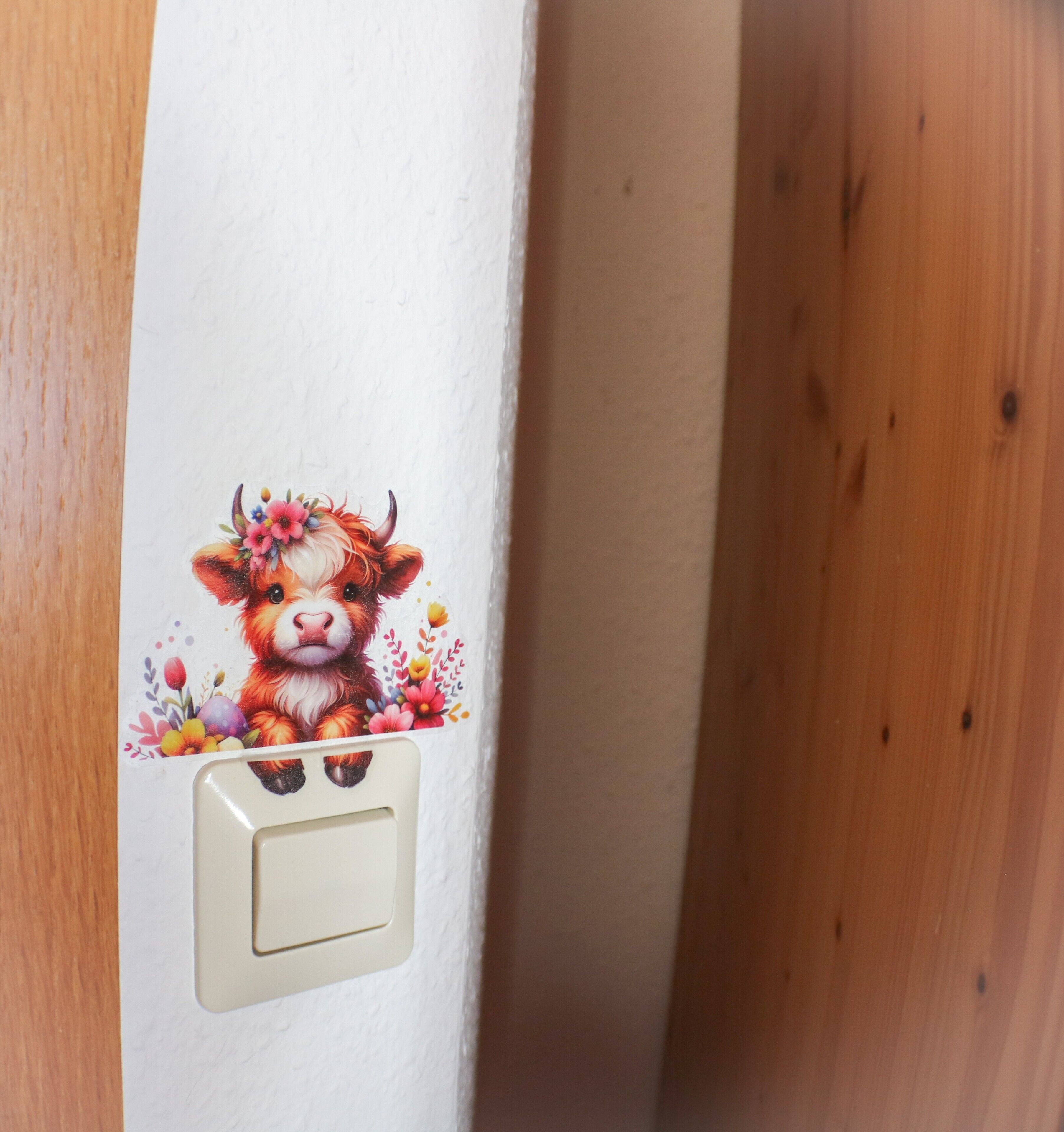 Un mur avec un interrupteur et un autocollant décoratif représentant une vache entourée de fleurs.