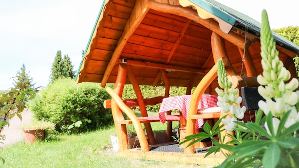 Uma cabana de madeira com telhado inclinado, um banco e uma mesa com toalha xadrez.