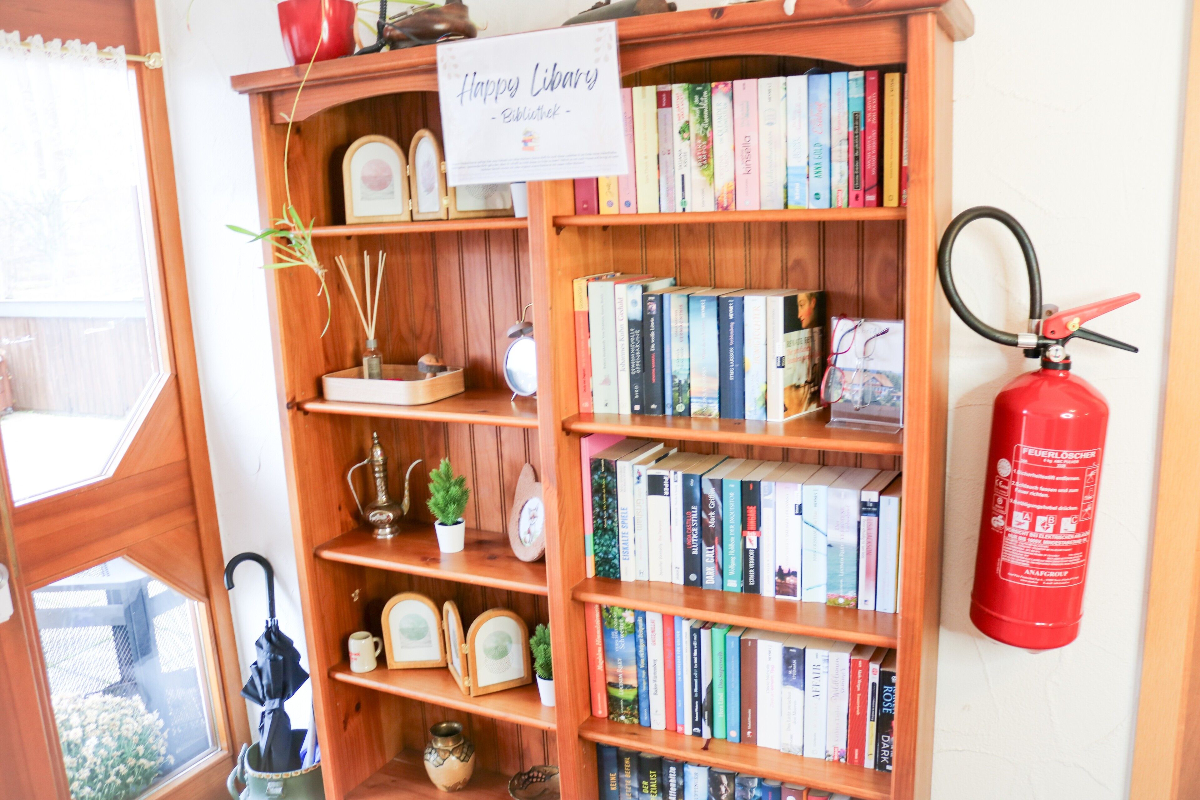 Ein Bücherregal mit Büchern, ein Feuerlöscher und ein Schild mit der Aufschrift 'Happy Library'.