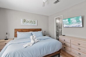 Ein Schlafzimmer mit Bett, Holz-Kopfteil, Nachttisch, Kommode, einem Gemälde und einem Fernseher.