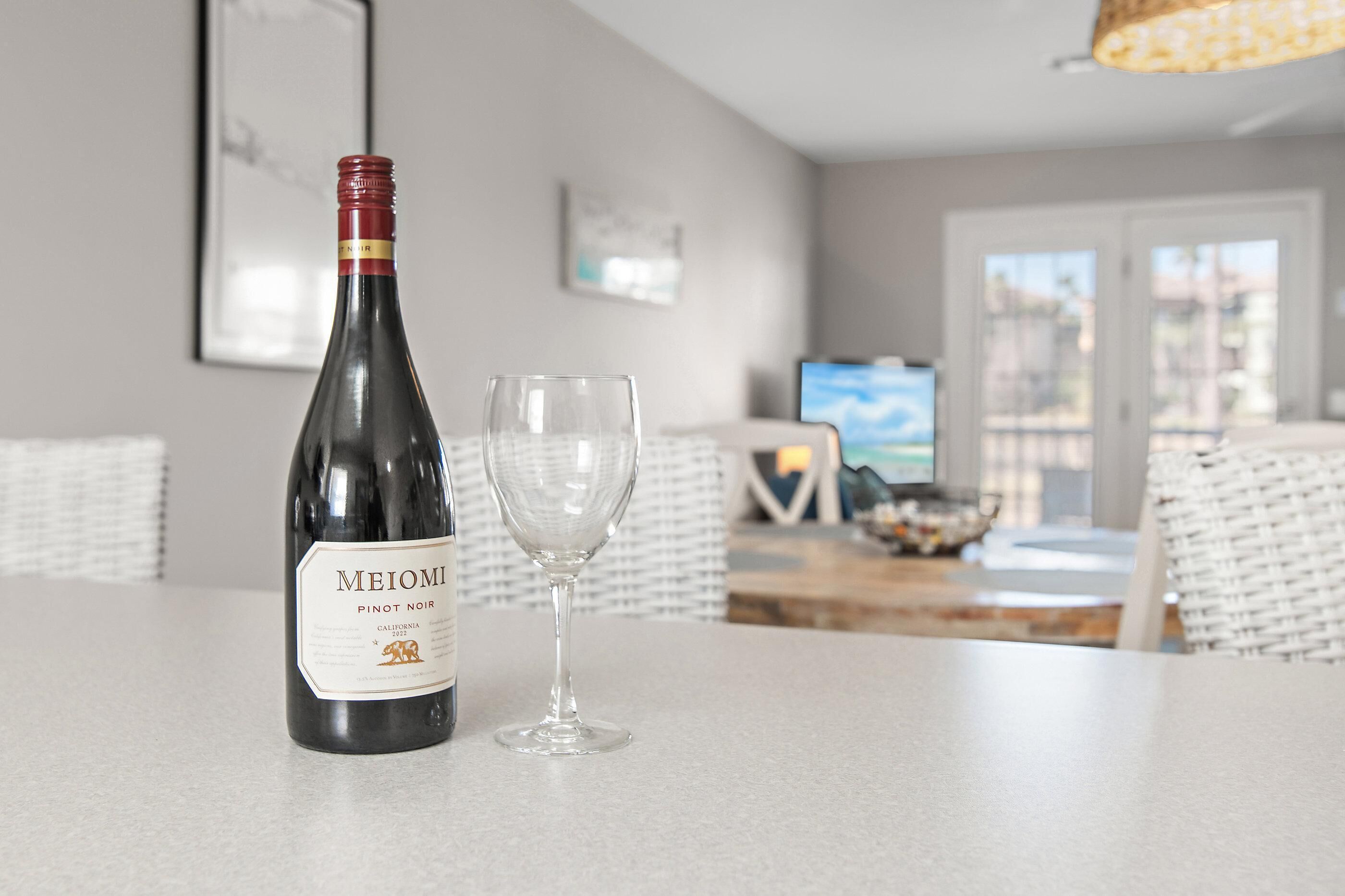 En flaske Meilomir Pinot Noir og et tomt vinglas på et bord i en moderne stue med et fjernsyn og udsigt til det fri.