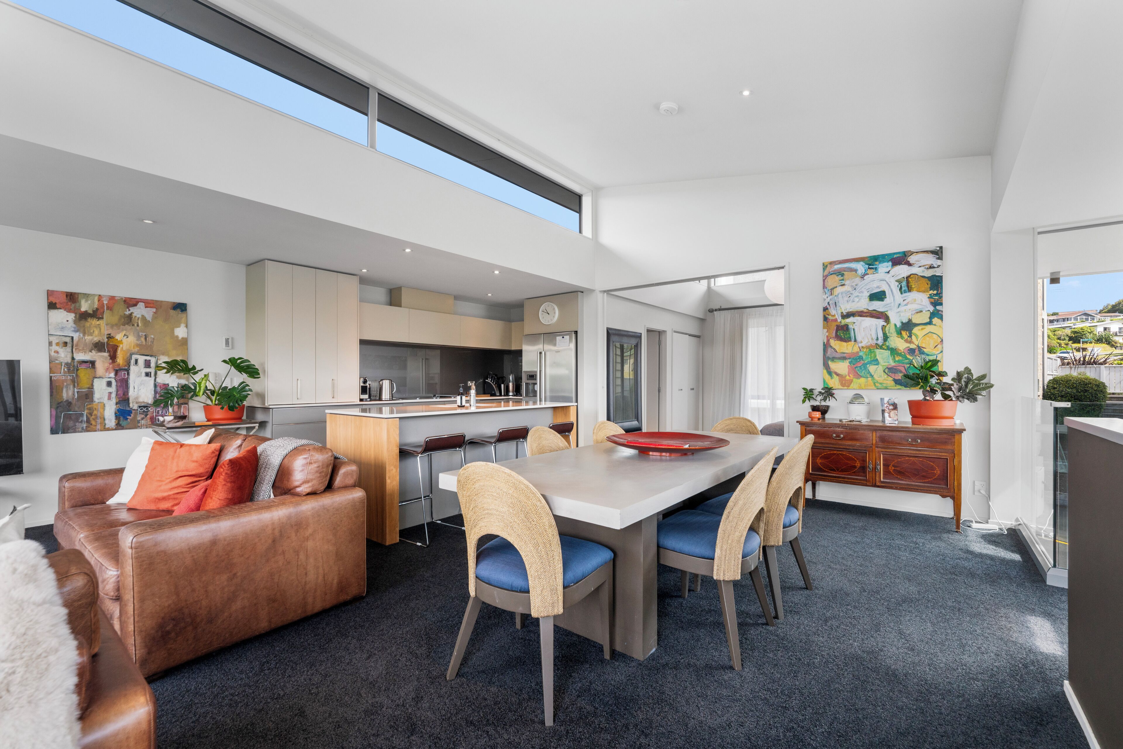 A modern open-plan living area with a dining table, sofas, and a kitchen in the background.
