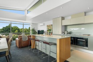 Una cocina moderna con una isla grande, taburetes de bar y un comedor con sofá y mesa.