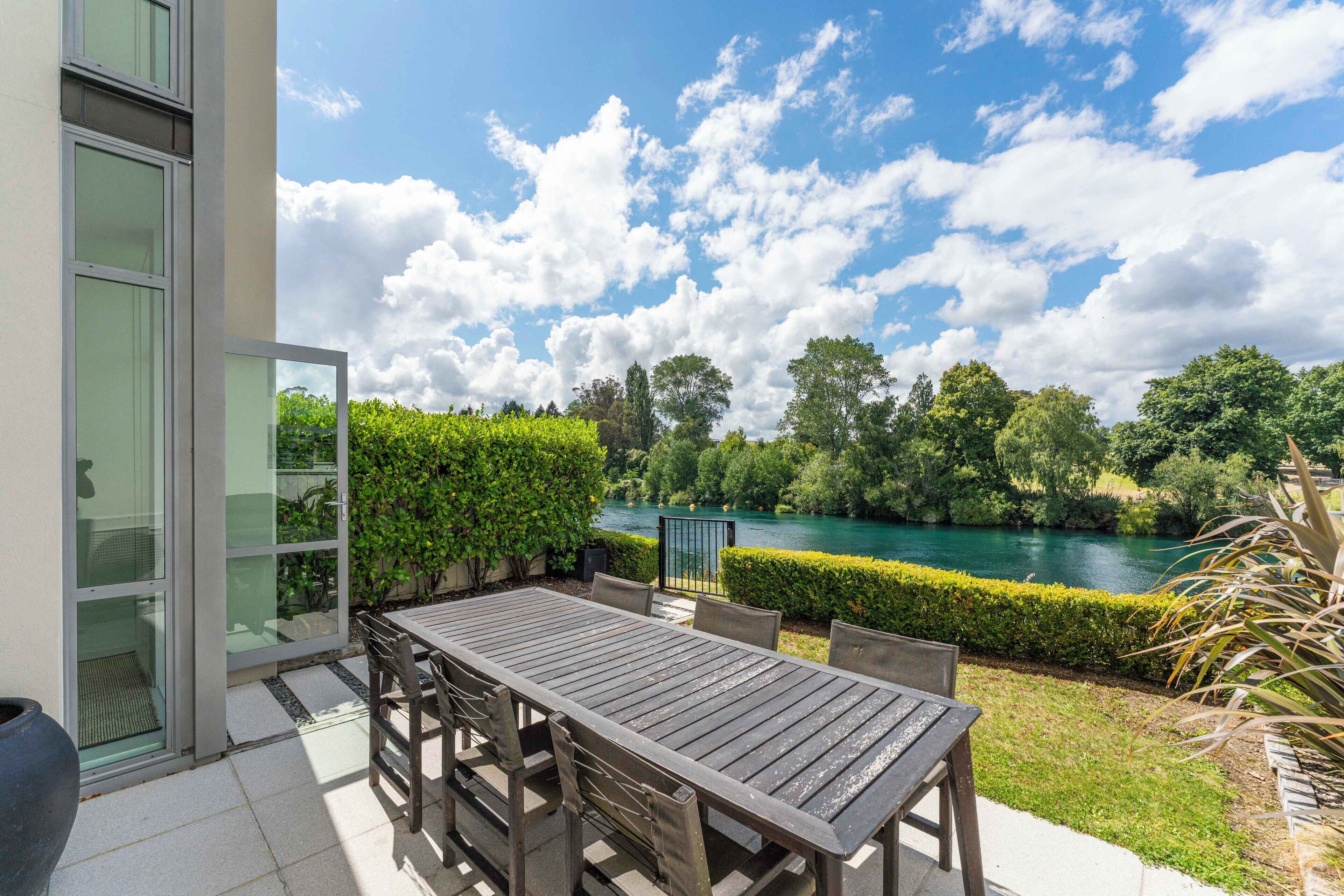 Eine Terrassenanlage im Freien mit Tisch und Stühlen, mit Blick auf einen Fluss und viel Grün.