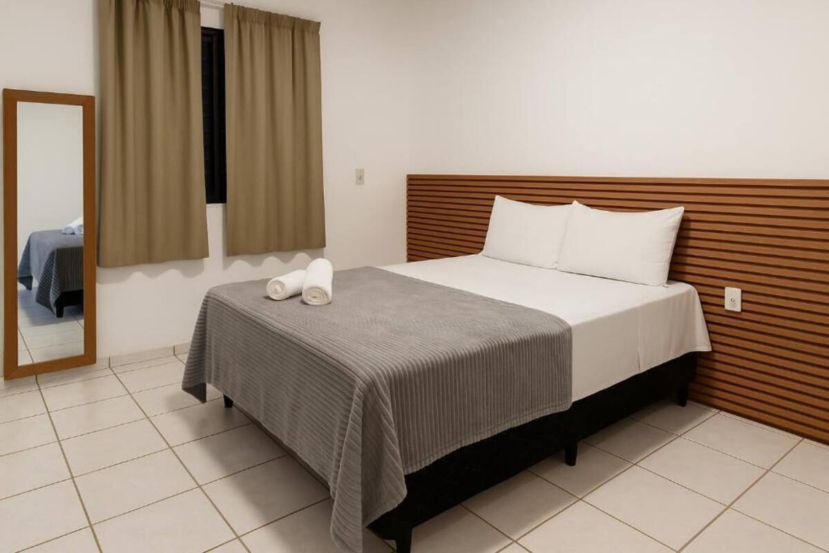 A single bed with a wooden headboard, a grey bedspread, and two white pillows.