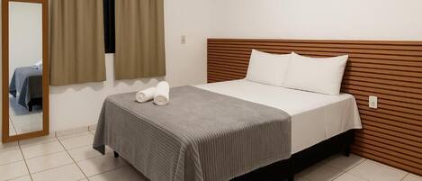Una cama individual con cabecera de madera, una colcha gris y dos almohadas blancas.