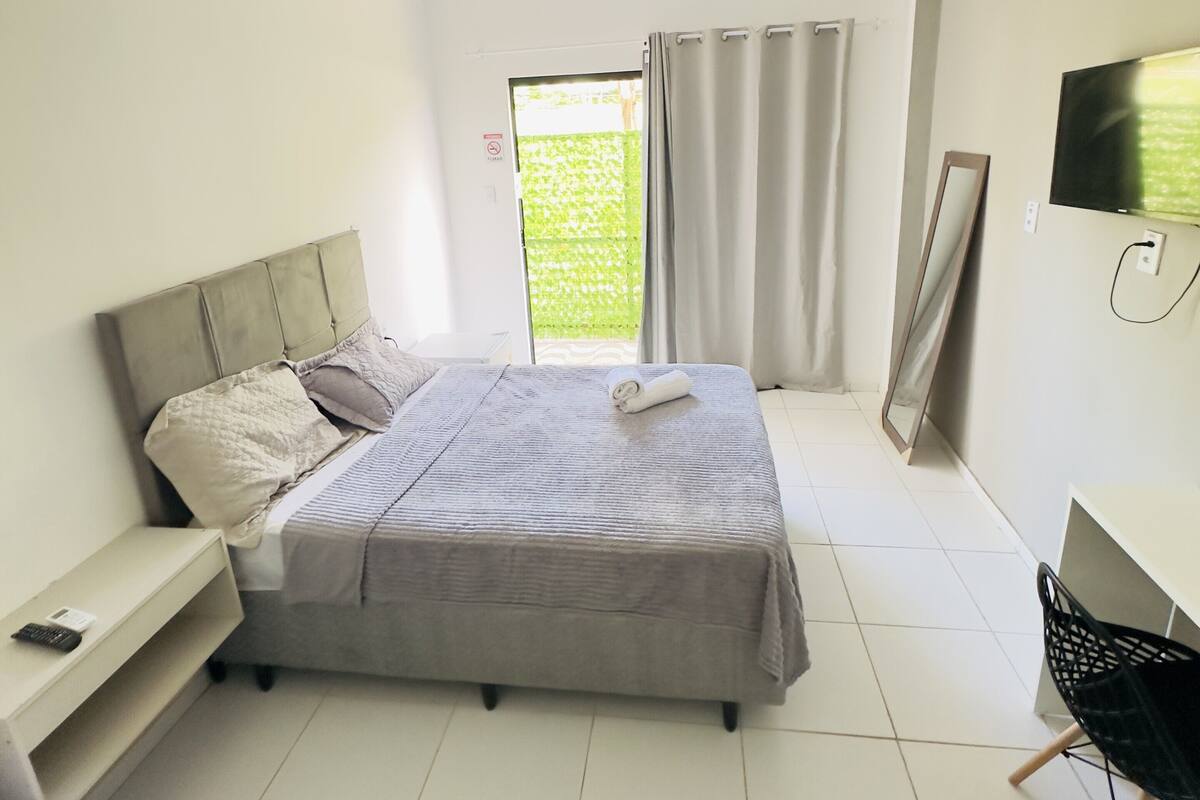 A bedroom with a bed, bedside table, TV, and a desk.