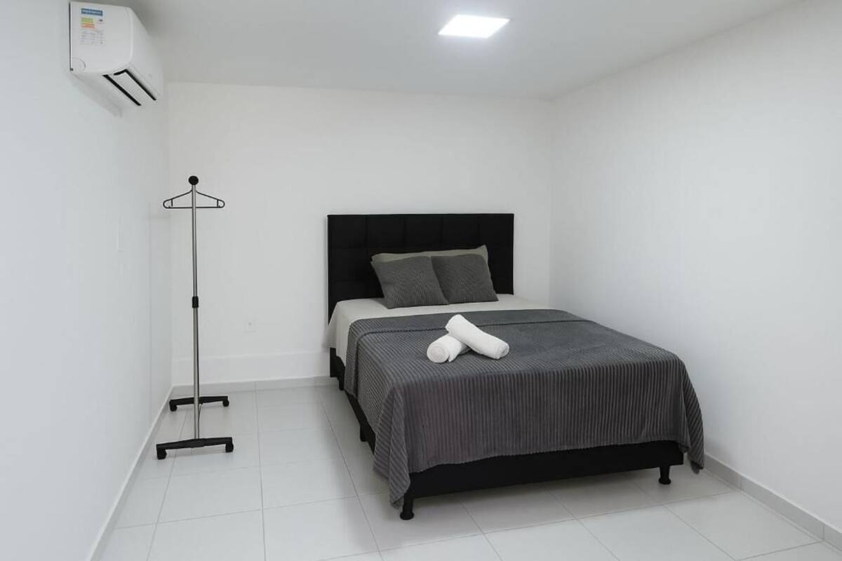 A bedroom with a bed, a floor lamp, and an air conditioning unit.