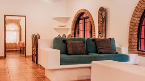 Una sala de estar con un sofá blanco, cojines verdes, un ventilador de techo y piso de baldosas.