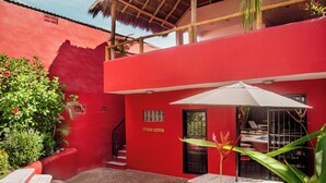 Un edificio rojo con piscina, una mesa con sombrilla y una escalera.