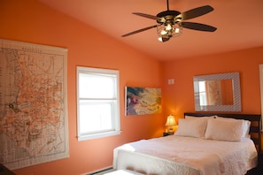 Une chambre à coucher avec un lit, un ventilateur de plafond, une carte accrochée au mur, une fenêtre et un tableau.