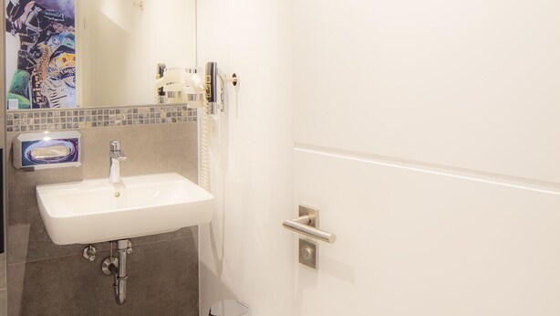 A modern bathroom with a white sink, mirror, and tiled walls. - Hotel Zur Feldmühle  (Arnsberg)