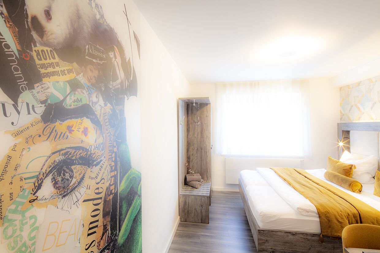 Un dormitorio con cama, un banco de madera, una ventana con cortinas y una pared con un collage de imágenes y texto.