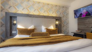 A modern bedroom with a geometric patterned wall, a large bed with brown bedding, and a flat-screen TV mounted on the wall. - Hotel Zur Feldmühle (Arnsberg)