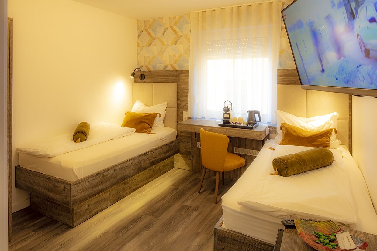 Une chambre d’hôtel avec deux lits, un bureau, une chaise et un téléviseur.
