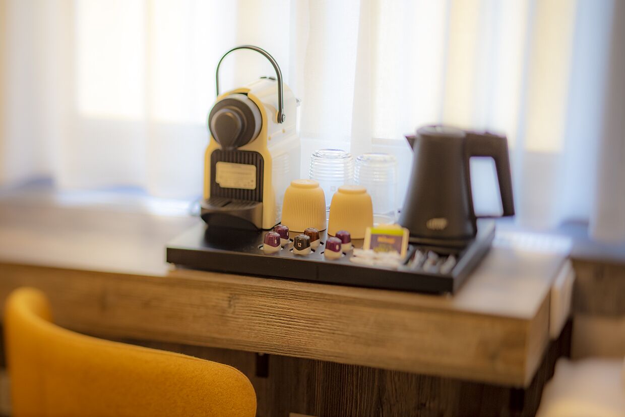 Una cafetera, espumador de leche y tazas de café sobre una mesa de madera en una habitación con ventana.