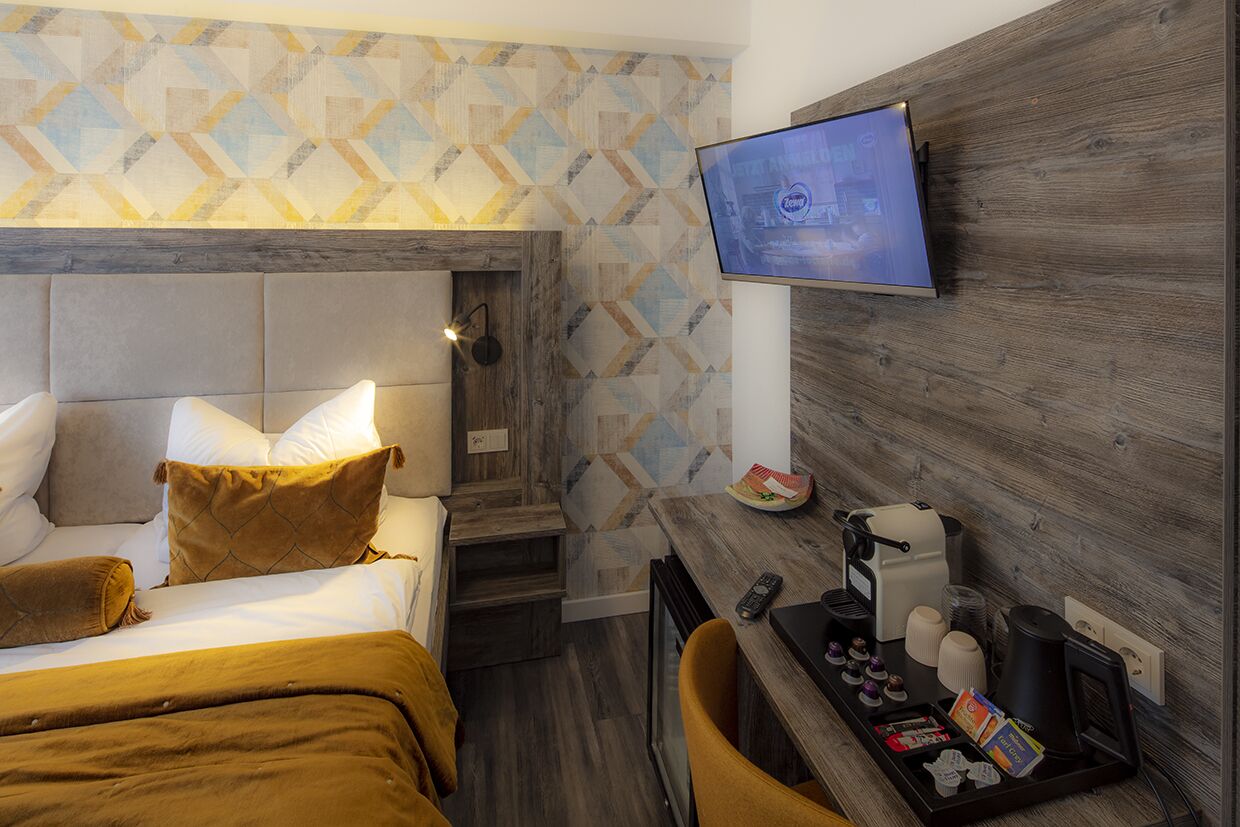 Habitación de hotel con cama, televisor montado en la pared, cafetera y bandeja con artículos de aseo.