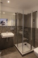Un baño moderno con ducha envuelta en vidrio, un lavabo blanco y un salpicadero de azulejos.
