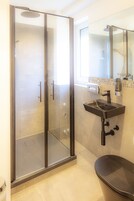 Un baño moderno con ducha acristalada, un lavamanos negro y un inodoro.