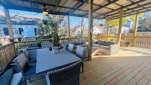 En overdækket terrasse med spisebord og stole, omgivet af fletningsmøbler og krukkeplanter.