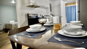 Une table à manger dressée avec des bols et des assiettes blancs, une chaise en bois, et une cuisine en arrière-plan.