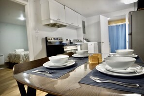 A dining table set with white bowls and plates, a wooden chair, and a kitchen in the background.