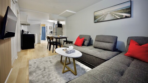Un salon moderne avec un canapé gris, des coussins rouges, une petite table ronde et un tableau accroché au mur.