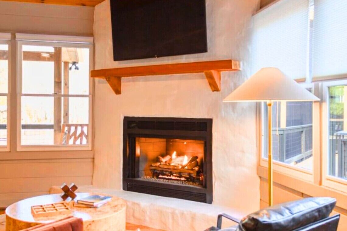 A cozy room with a fireplace, a television mounted on a wooden beam above it, and a table with a cross-shaped decoration.