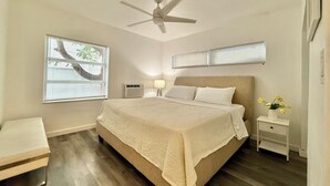Ein Schlafzimmer mit Bett, Deckenventilator, Nachttisch, Lampe und Fenster mit Jalousien.