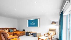 Una sala de estar moderna con un sofá de cuero marrón, una mesita de madera, una obra de arte con marco azul y una lámpara.