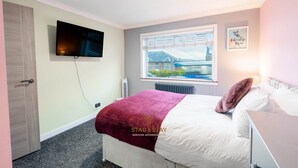 Un dormitorio con cama, televisor montado en la pared, ventana con vistas y radiador.