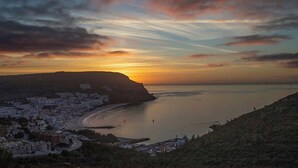 Une ville côtière caractérisée par une colline imposante, une plage et une mer calme au coucher du soleil.