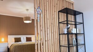 Une chambre avec un lit, une cloison en bois, une étagère noire et un luminaire suspendu.