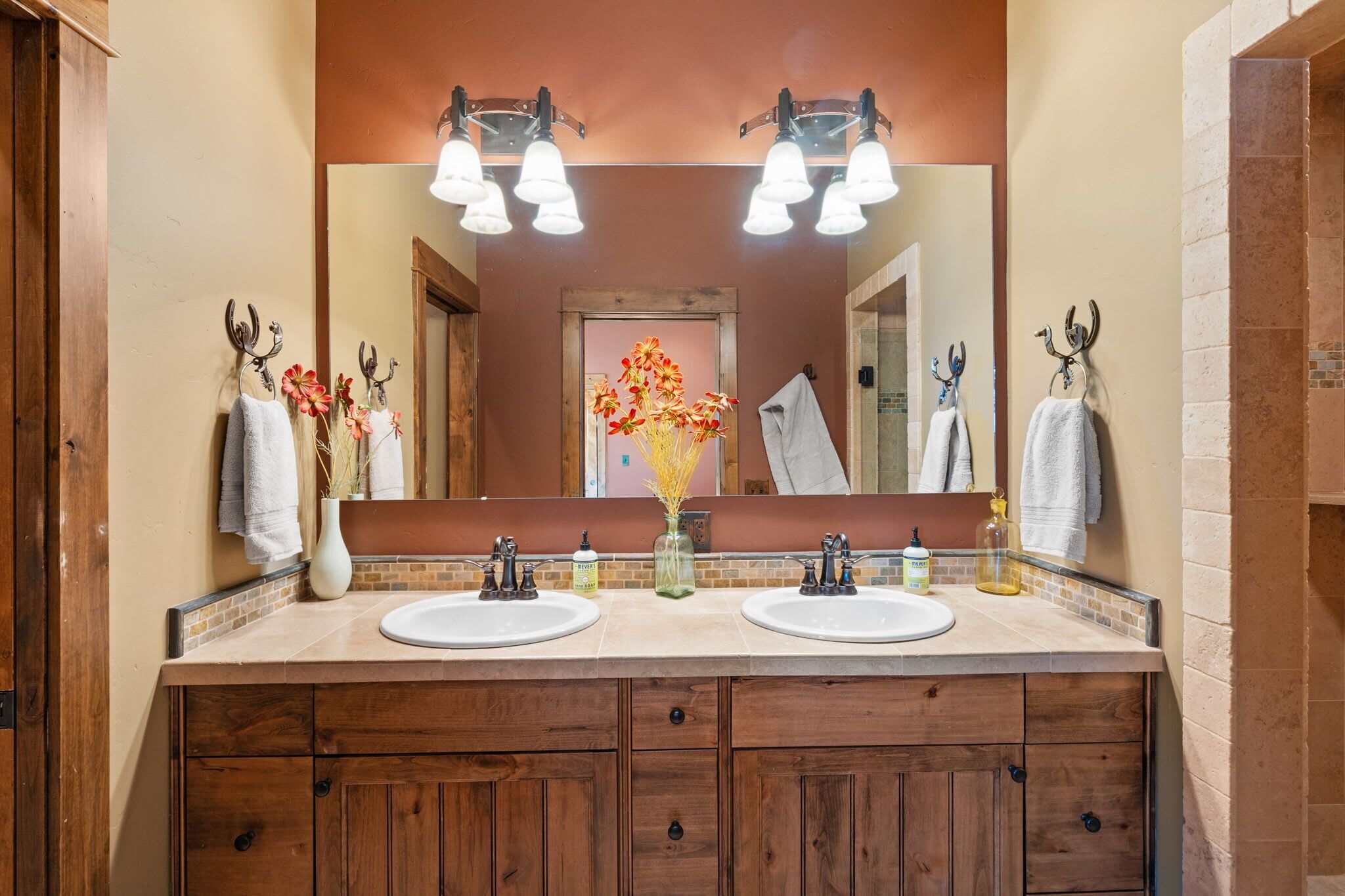 Une salle de bain avec deux lavabos, un grand miroir et un vase de fleurs.
