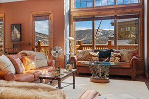 Ein gemütliches Wohnzimmer mit Ledersofas, einem Couchtisch und einem großen Fenster mit Blick auf die Berge.