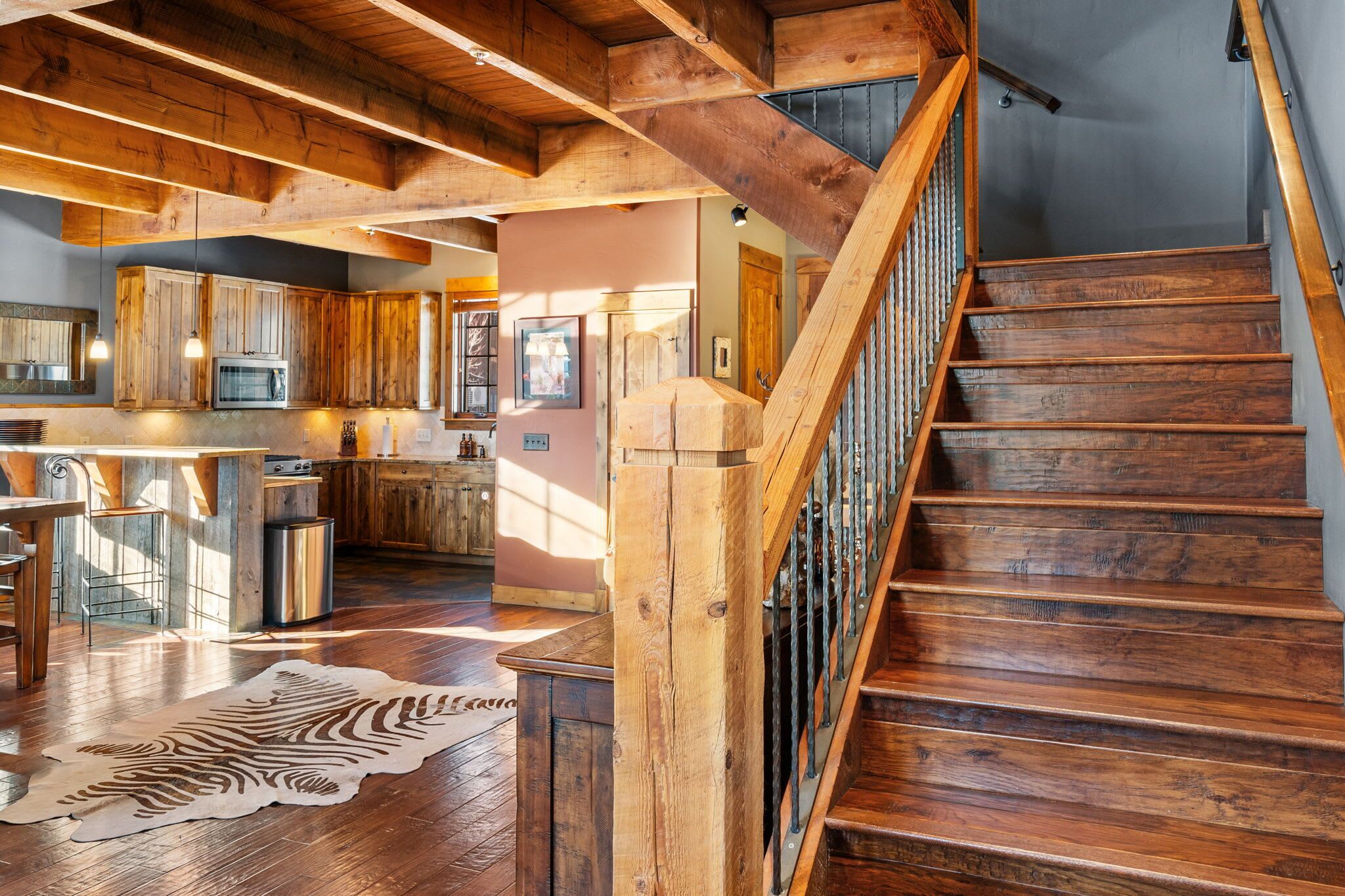 Une cuisine spacieuse avec des meubles de rangement en bois, un îlot central et un escalier doté d’une rampe en bois.