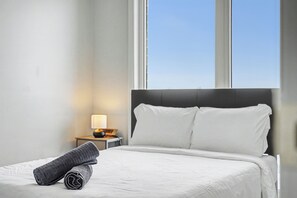 A neatly made bed with white linens, a grey towel, and a nightstand with a lamp. - Cedar Nest - 5 Beds, 3.5 Baths, 2 Park, Backyard (Pickering)